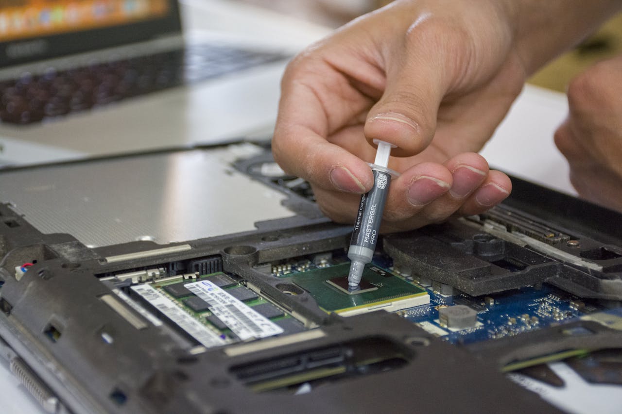 Surriscaldamento: Perché pulizia e cambio pasta termica salvano il tuo PC Close-up of hand applying thermal paste to a laptop microchip for maintenance.